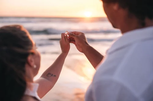 Anais and Quinn holding up the engagement ring at sunset on the beach