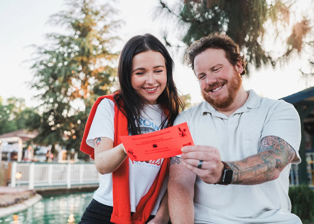 Hannah and Tylor laughing over a red ticket by the pond at the mini golf course