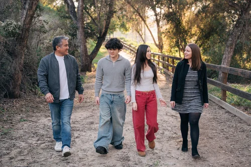 A family of four walking side by side down the fence-lined path at Oso Parkside Path in Laguna Hills