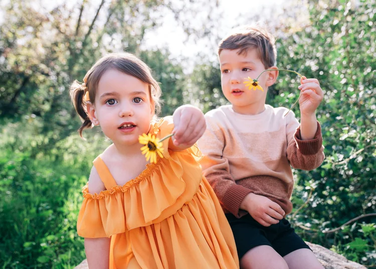 A young girl in a yellow dress holding a flower beside her brother during a family session
