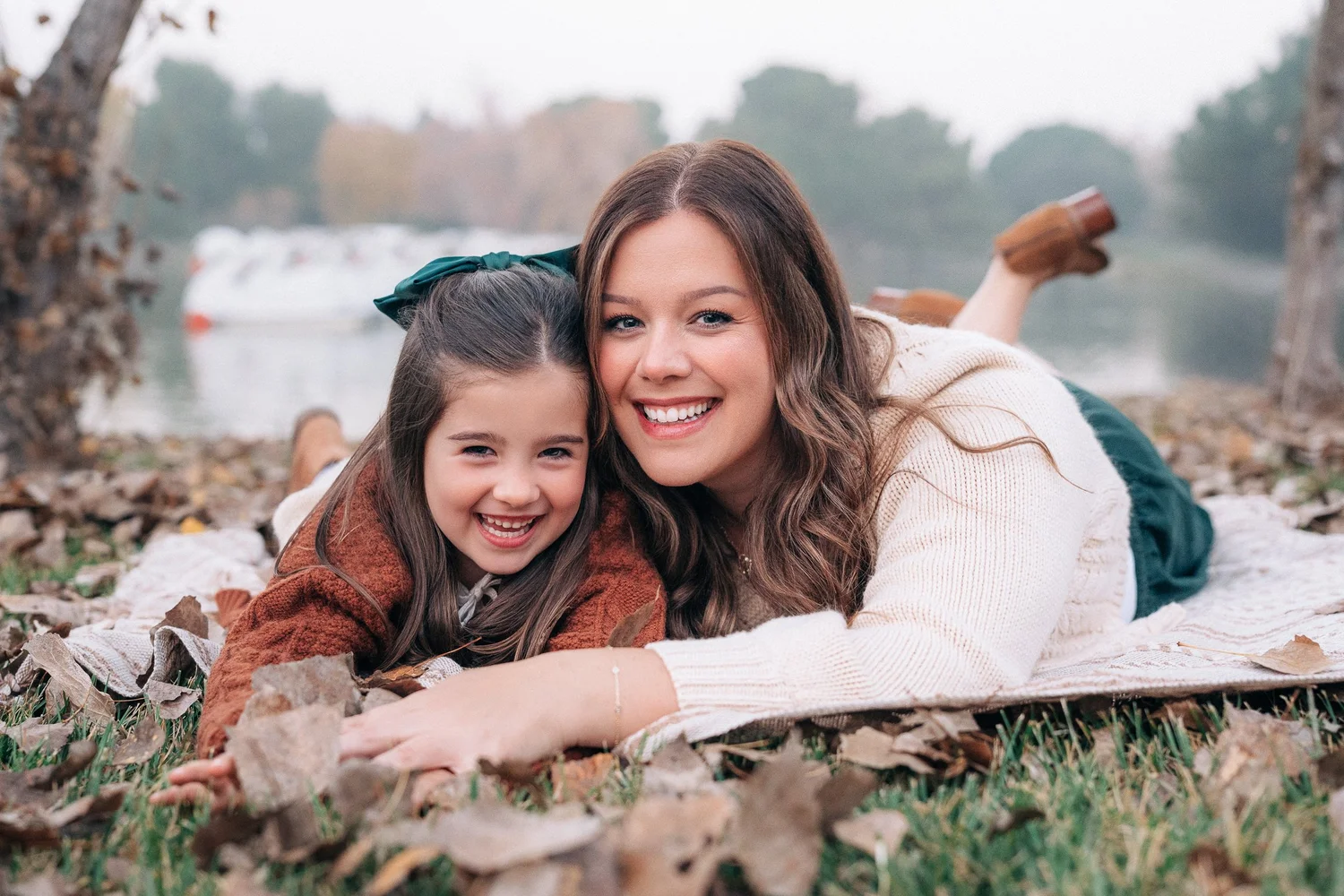 Mother and daughter lying back in the fallen leaves beside the water at an Orange County family session