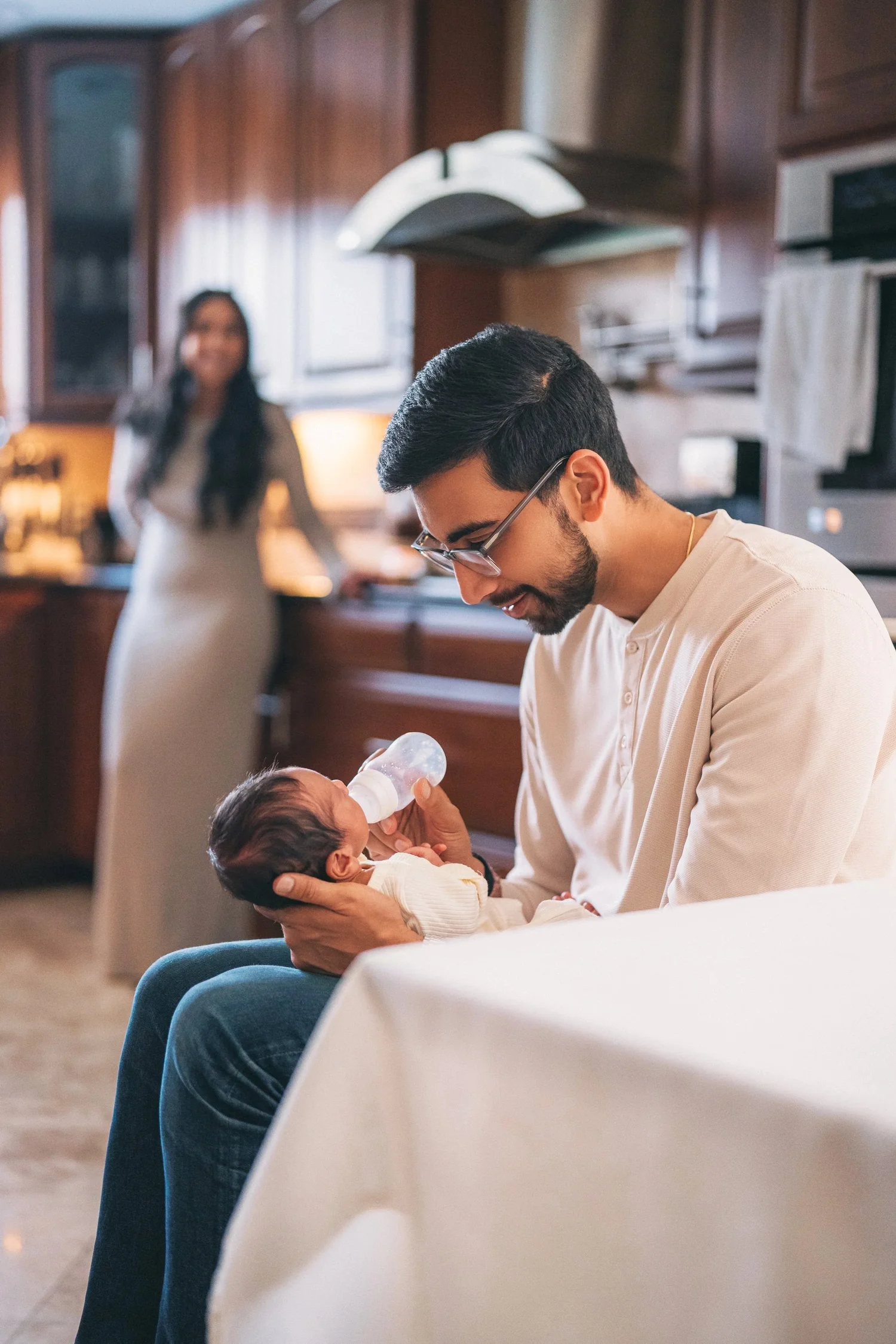 Father in a cream cardigan giving his newborn a bottle in the kitchen, in-home newborn session in Orange County