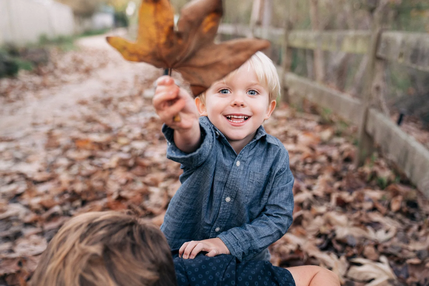 Close-up of a grinning toddler holding a leaf, photographed from ground level during an Orange County family session