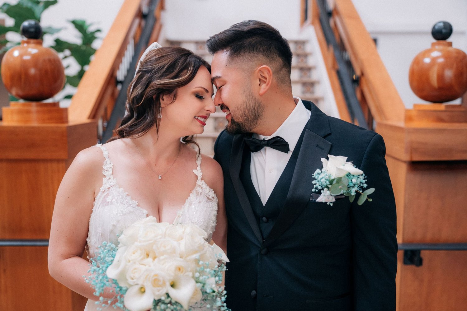Jessica and Alex forehead to forehead on the courthouse staircase, she holds a white bouquet