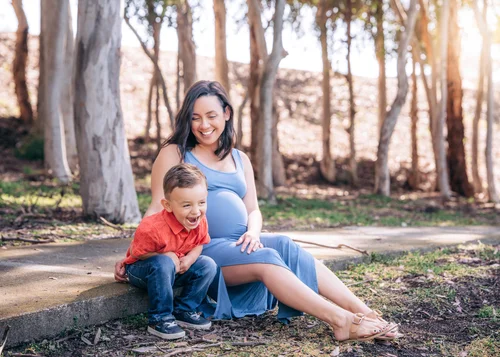 A mom sitting on the path laughing with her young son among the eucalyptus trees at Serrano Creek Park