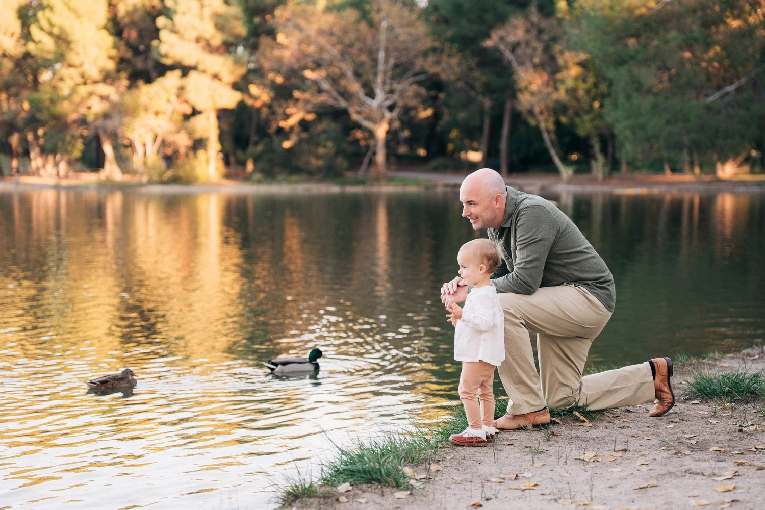 A parent and small child at the water's edge at Yorba Regional Park, gold trees reflected in the lake behind them