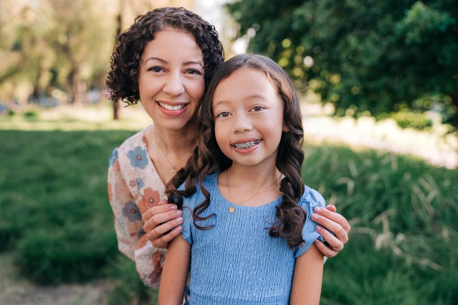 Mom and her younger daughter smiling together, Mom's hands resting on her shoulders