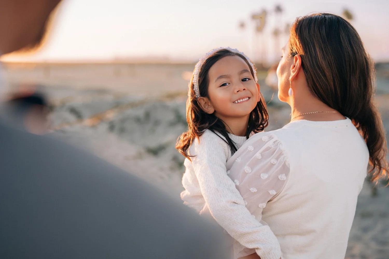 A mother holding her daughter at golden hour on the sand dunes at Seal Beach