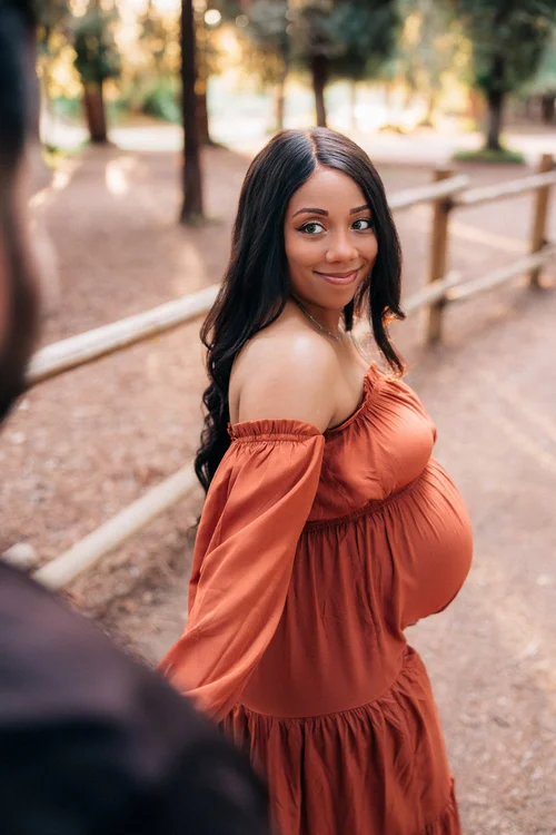 Mom glancing back over her shoulder in a rust off-the-shoulder dress on the redwood path