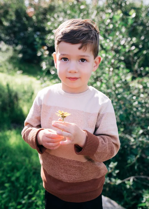 The Leon son holding a single yellow daisy in both hands, looking straight at the camera