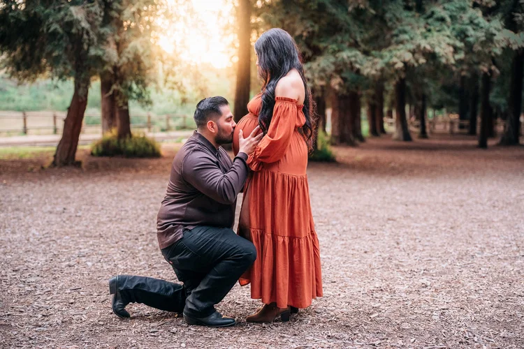 A dad-to-be kneeling to kiss the bump at golden hour during a maternity session in Brea