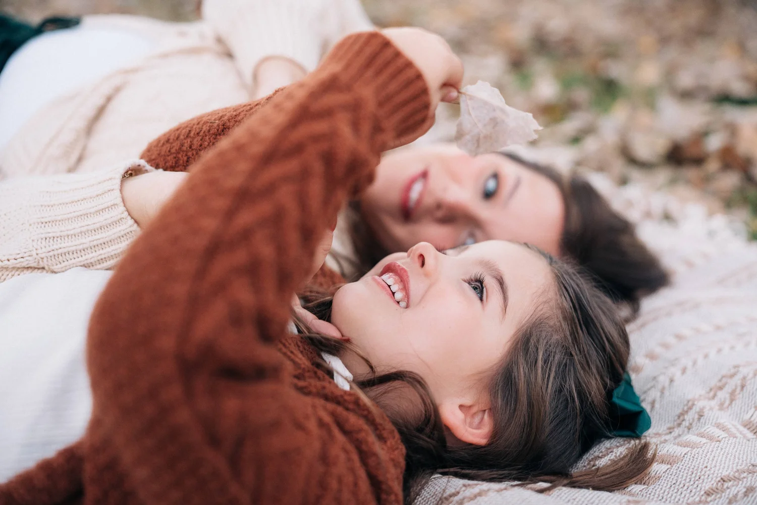Mother and daughter lying in the leaves, laughing together, at an Orange County family session