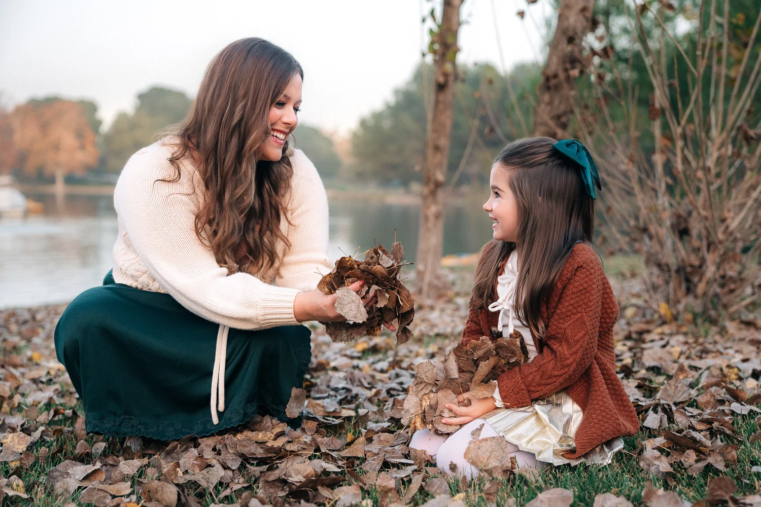 A mother and daughter sitting together in the fallen leaves on the lake bank at Yorba Regional Park