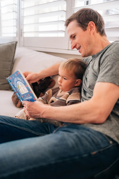 Dad reading a book to his son on the couch during an in-home session in Irvine