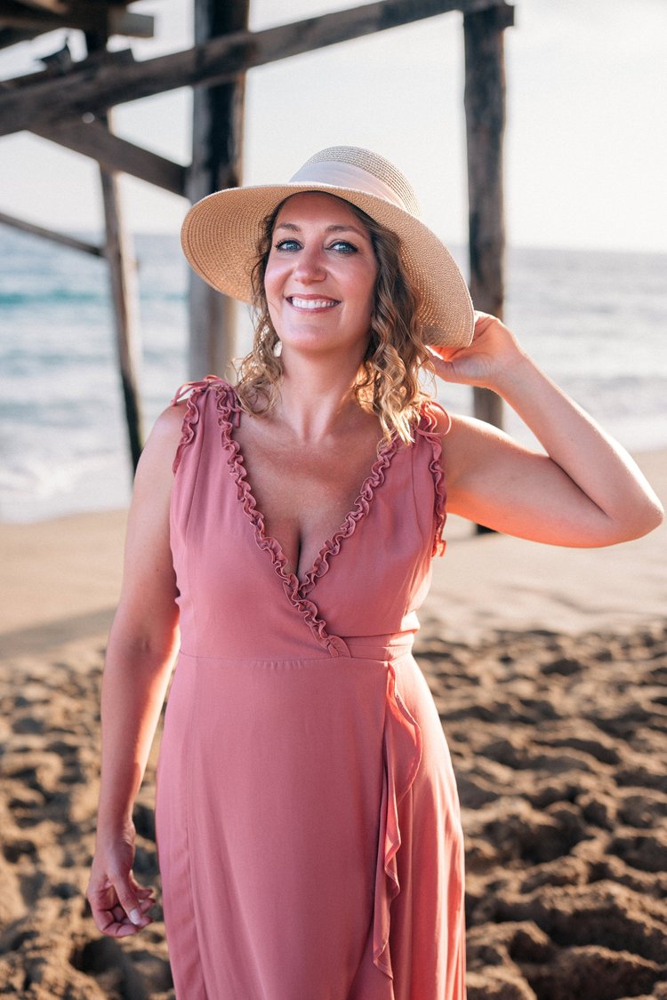 Mom in a sun hat and pink dress smiling under the pier at the beach