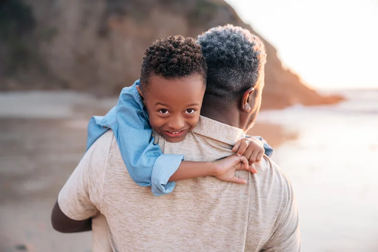 A young boy looking back over his father's shoulder while being carried along the beach