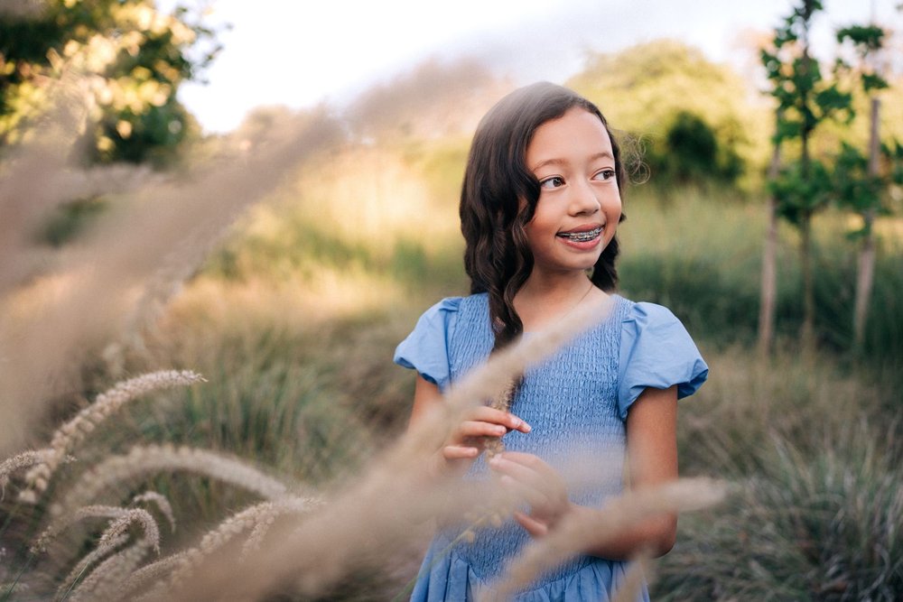 The younger Slemmons daughter in a blue dress standing in the tall grass at Jeffrey Open Space Trail