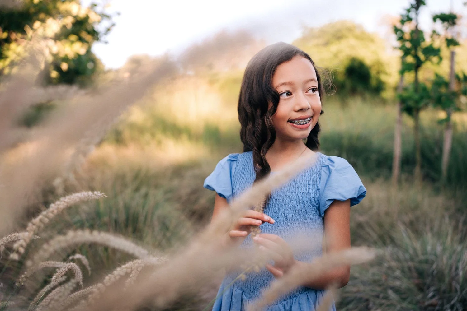 The younger Slemmons daughter in a blue dress standing in the tall grass at Jeffrey Open Space Trail