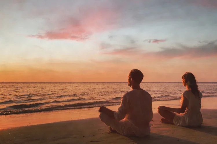 Two adults meditating on a beach at sunset