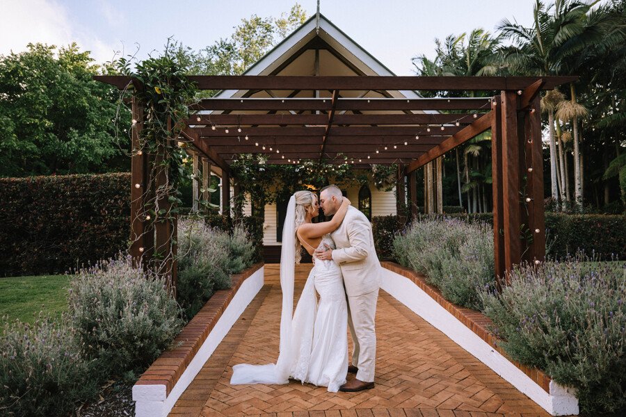 A wedding couple embracing beneath the garden pergola at Shambala Estate.