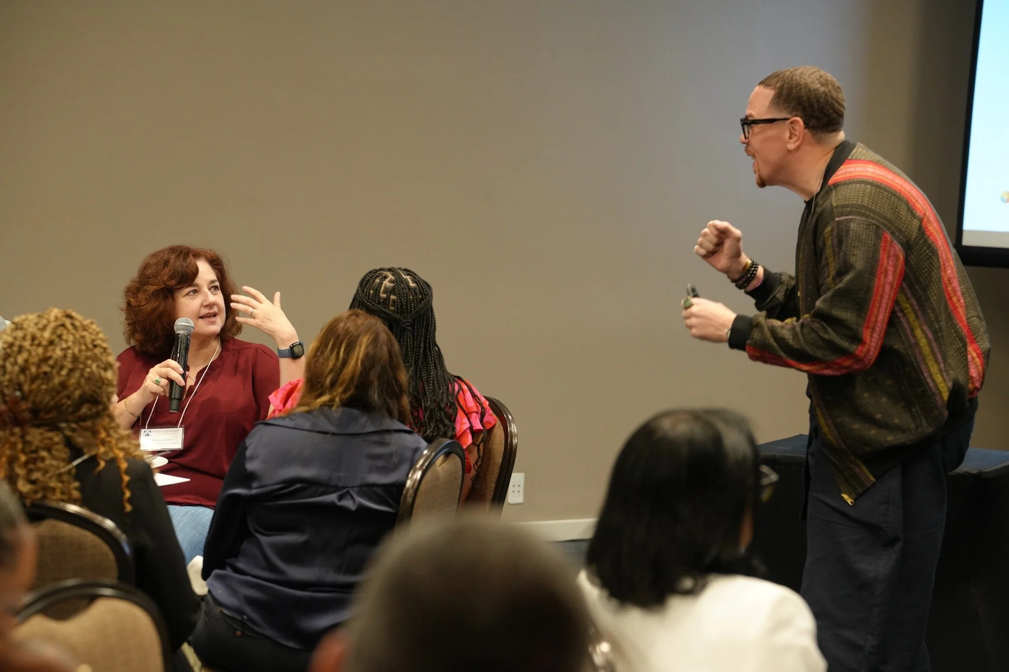 A participant speaks into a microphone as Sean Goode engages with her during a group discussion.