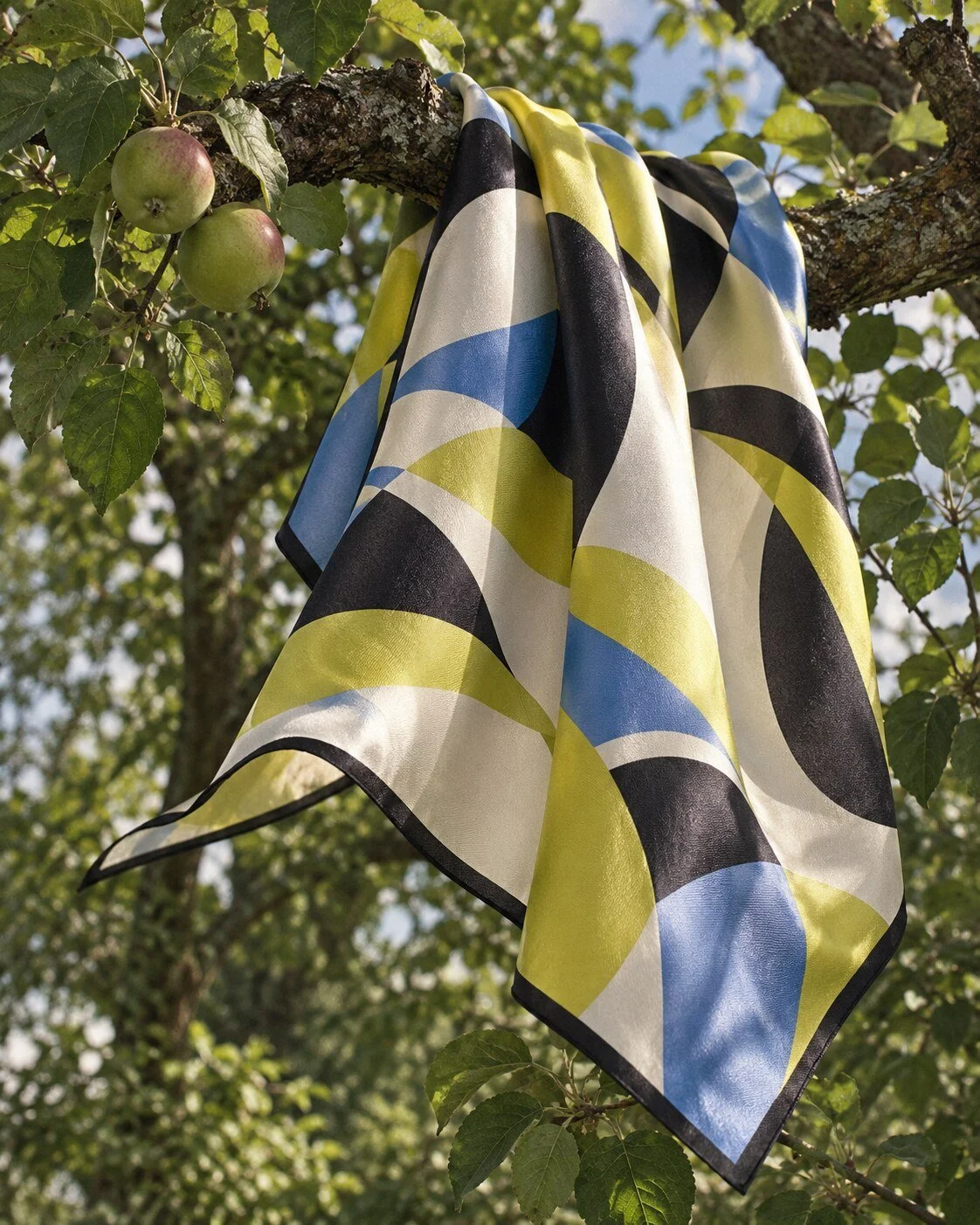 Yellow, blue, ivory and black geometric scarf draped over an apple-tree branch