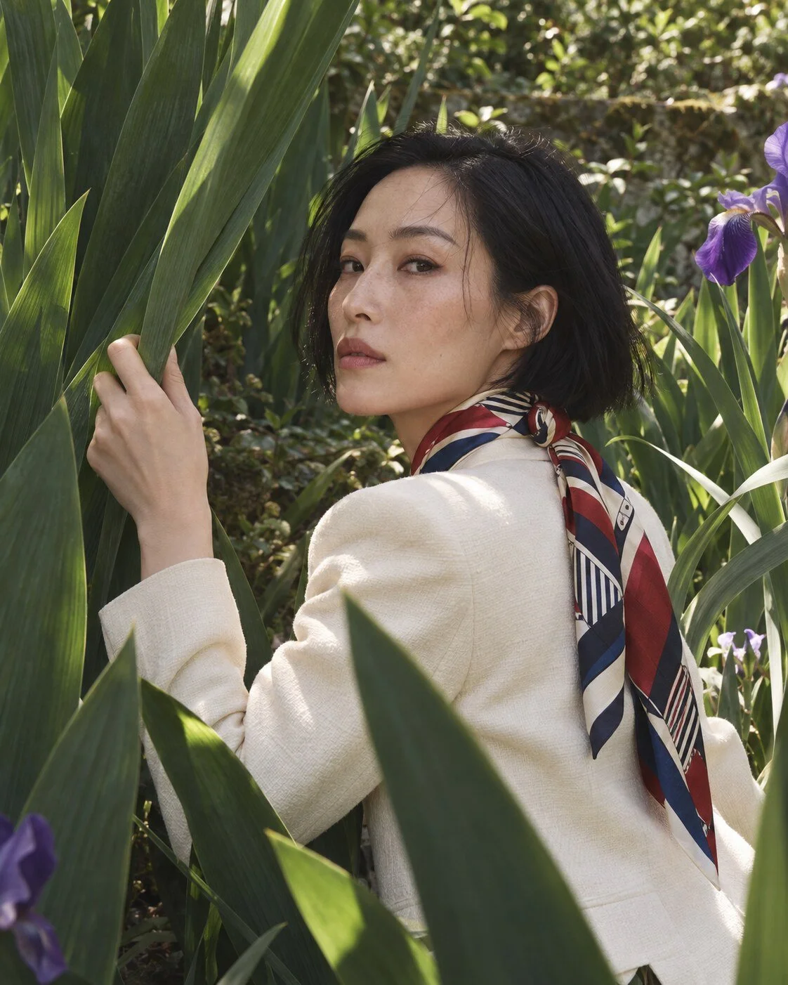 Woman wearing a red, navy and ivory graphic silk scarf among green iris leaves