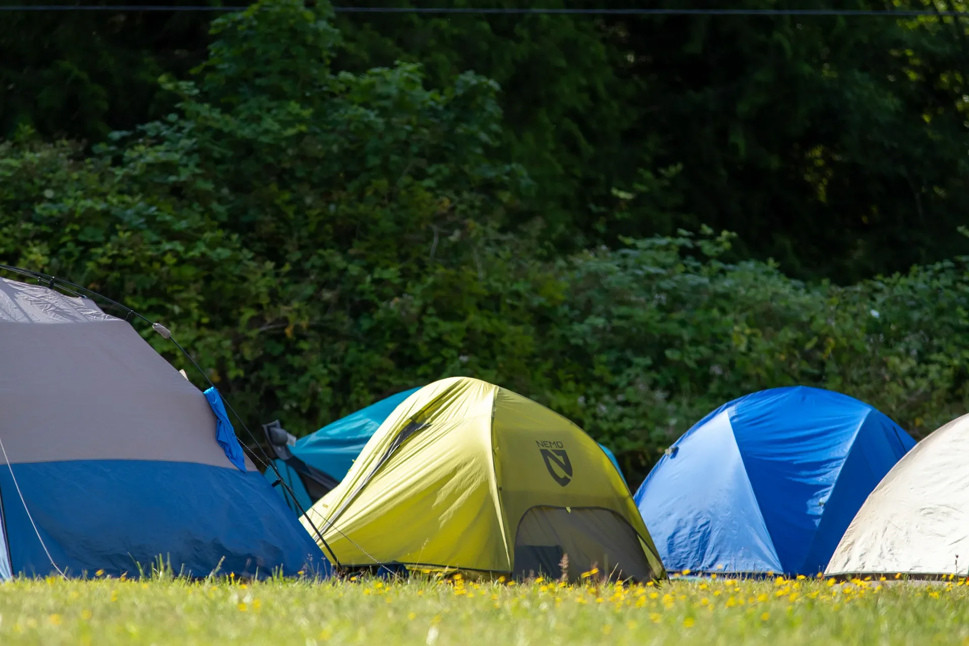 Close view of yellow, blue and gray tents on a grassy field under a cloudy sky.