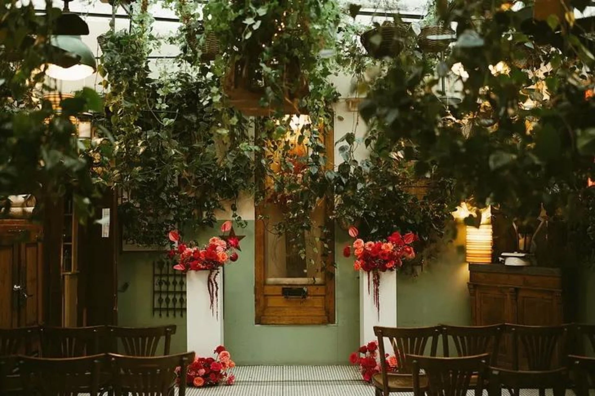 Indoor wedding ceremony setup with green walls and tall white pedestals topped with romantic red floral arrangements — Signature Experience by The Wedded Company, New York City.
