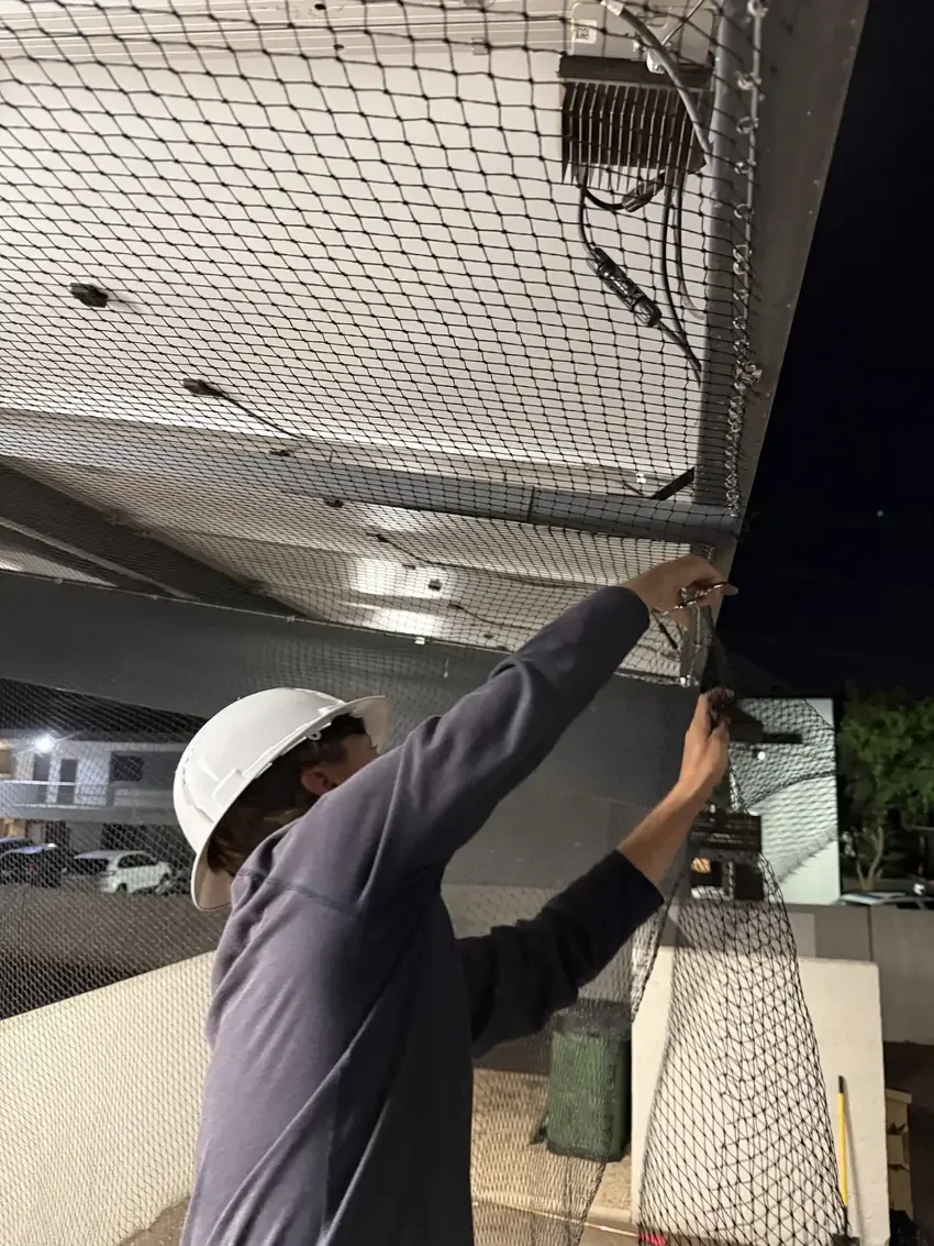 Installer fitting bird netting to an overhead structure.
