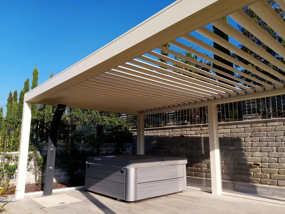 Una grande pergola bioclimatica in alluminio bianco che ospita una vasca idromassaggio e una doccia, all'interno di un lussuoso giardino a Roma.