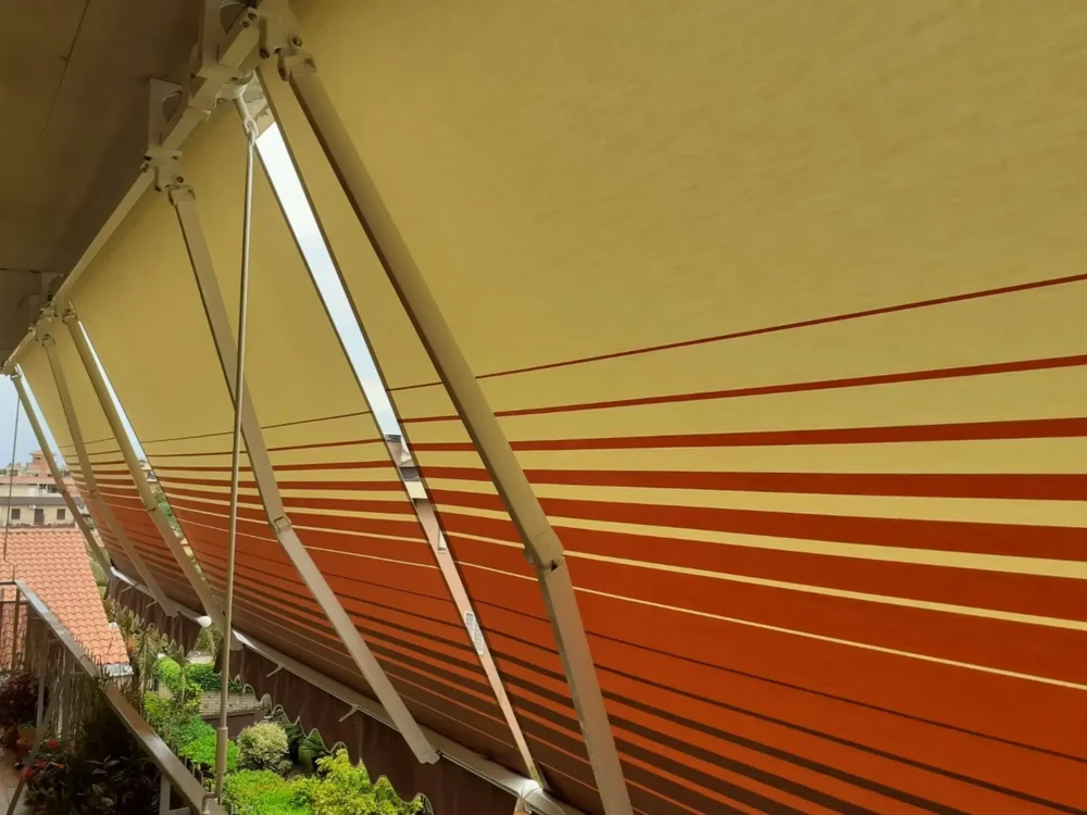 Una vista dettagliata dei bracci di una tenda da sole a strisce rosse in una giornata nuvolosa.