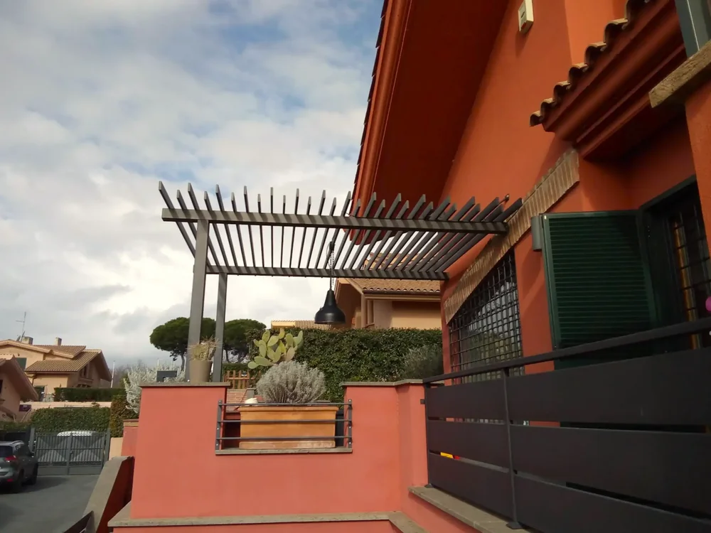 Una veranda dotata di un pergolato in legno color grigio che funge da luce per l'ingresso di una casa.