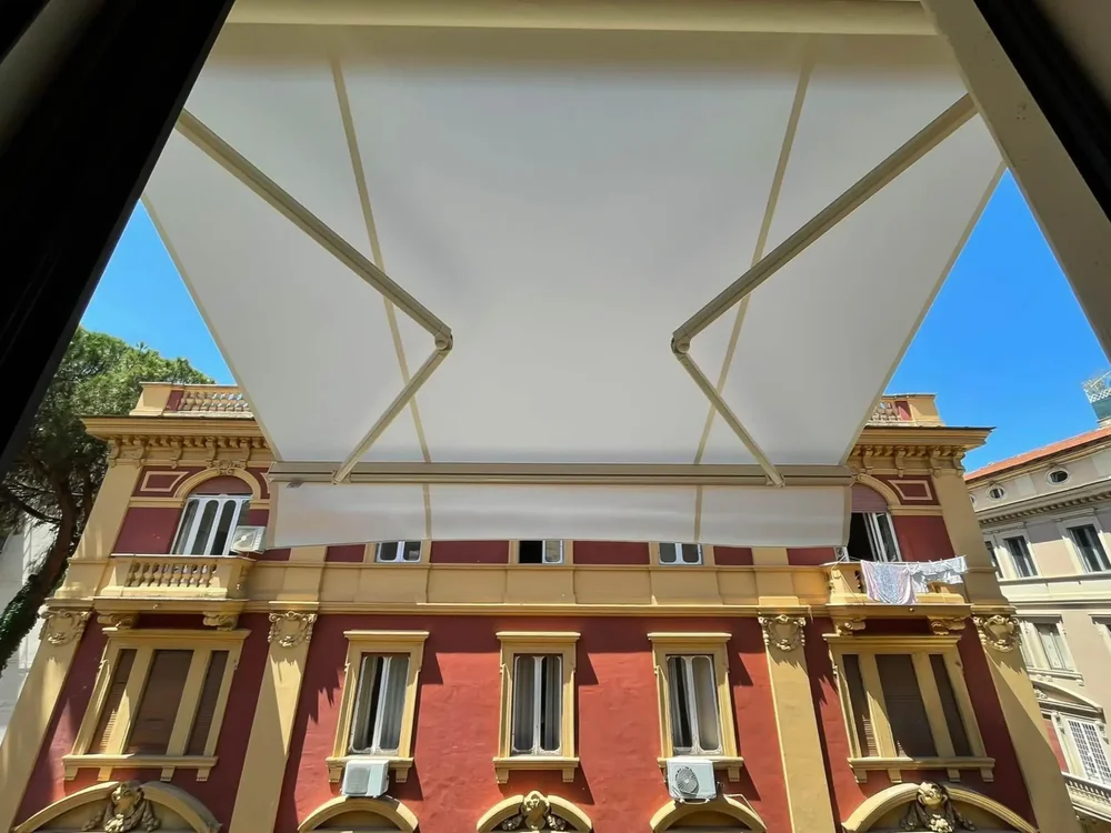 Sotto una tenda da sole estesa con bracci meccanici di fronte a un edificio storico.