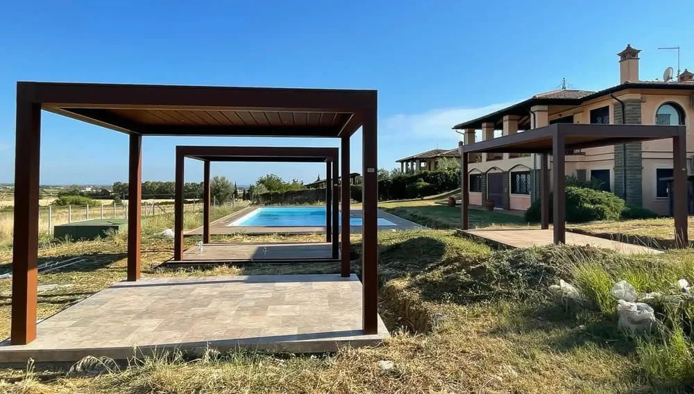 Tre pergole bioclimatiche metalliche di nuova costruzione con finiture scure che ricordano il legno, all'interno di un cortile con piscina a Roma.