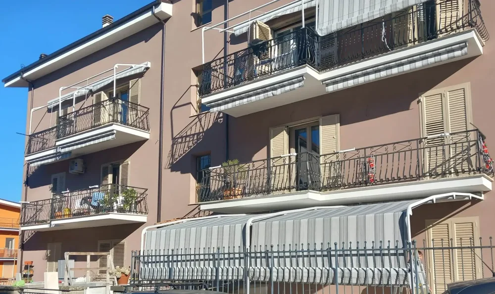 Esempi di tende da sole a capanno grigie installate su balconi a Roma, mostrate in posizione estesa e retratta per protezione antivento.