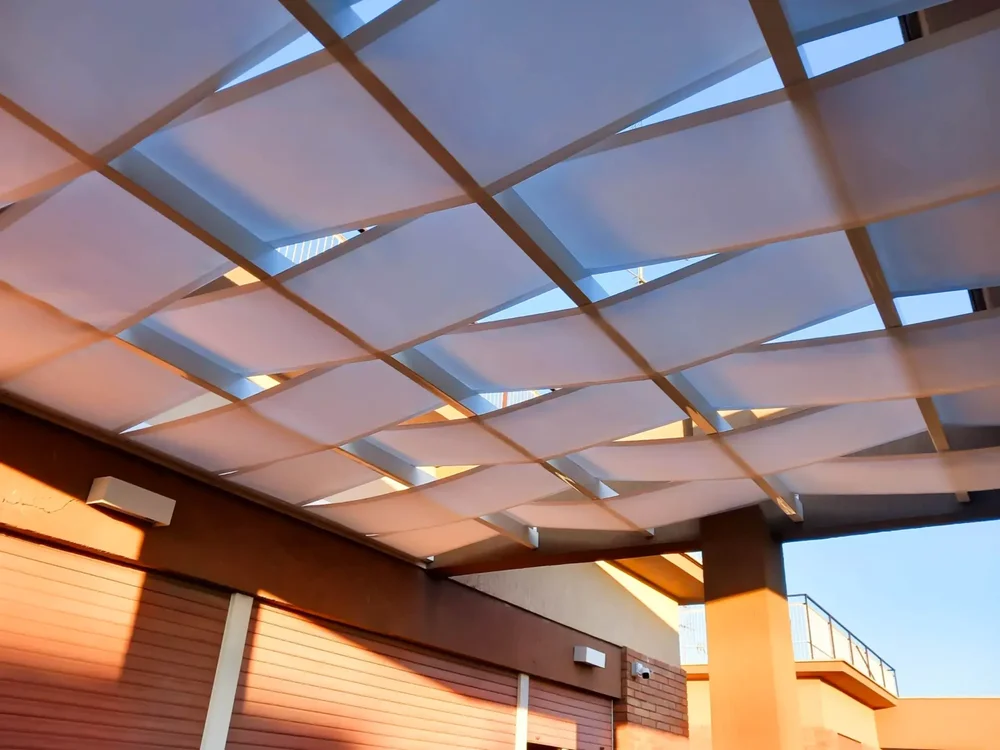 Una splendida pergola in legno realizzata con tessuto Tempotest bianco intrecciato, ideale per schermare il sole.