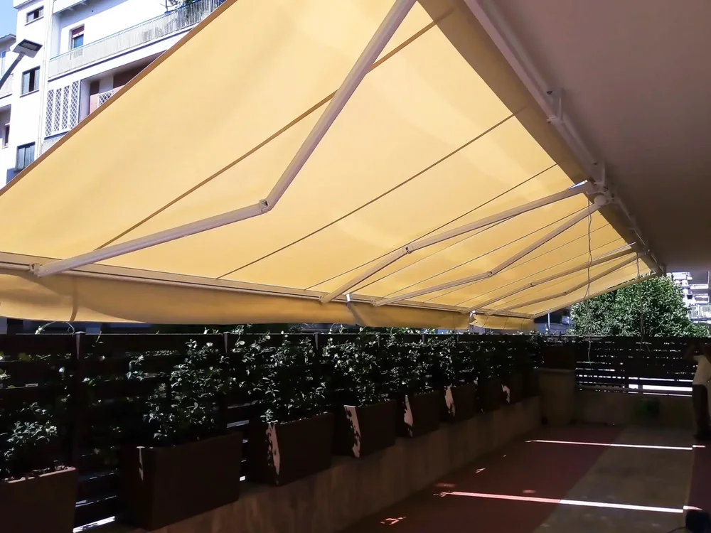 Terrazza moderna con tenda da sole in tessuto Tempotest giallo e tende a bracci motorizzate per la protezione solare.