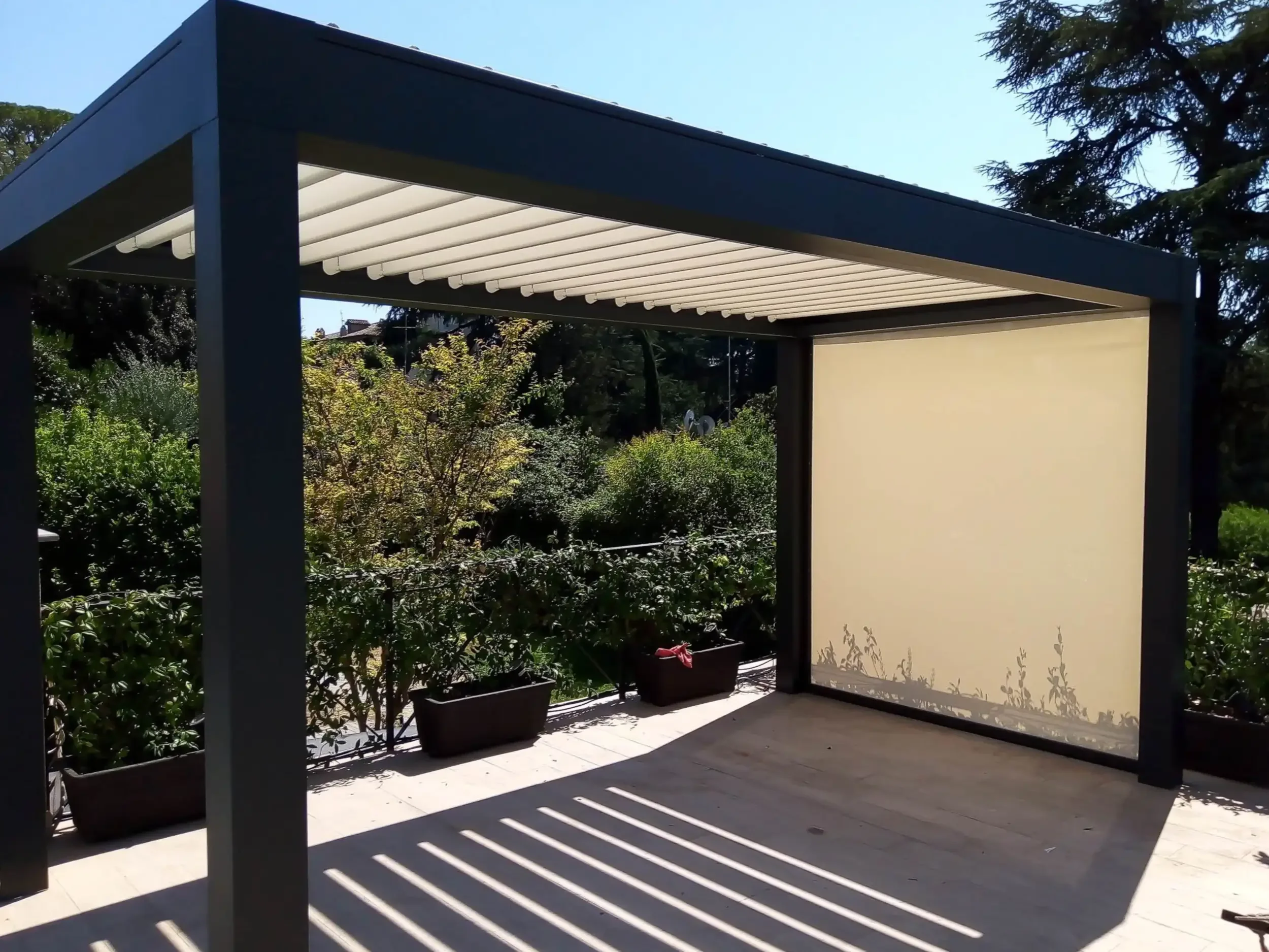 Una pergotenda in alluminio nero installata in un grande giardino.