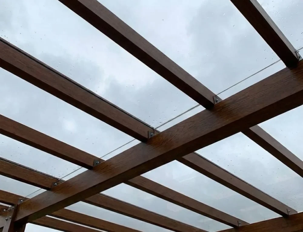 Vista inferiore del modello di una copertura in policarbonato di una tettoia in legno scuro che protegge dalla pioggia.