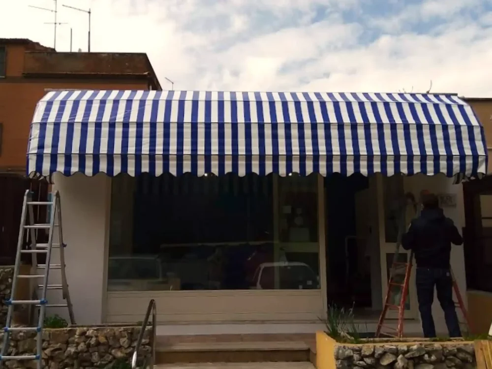 Vista frontale del processo di installazione della nostra cappottina in PVC a strisce blu e bianche sopra un ingresso