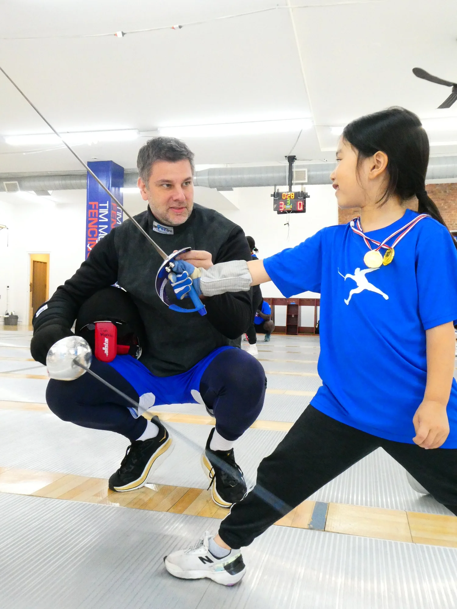 A TMFC coach sizing a young fencer for her mask and saber