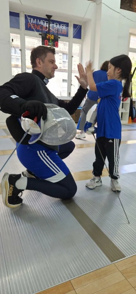 TMFC coach high-fiving a smiling young fencer after a fun first fencing lesson near Greenwich CT