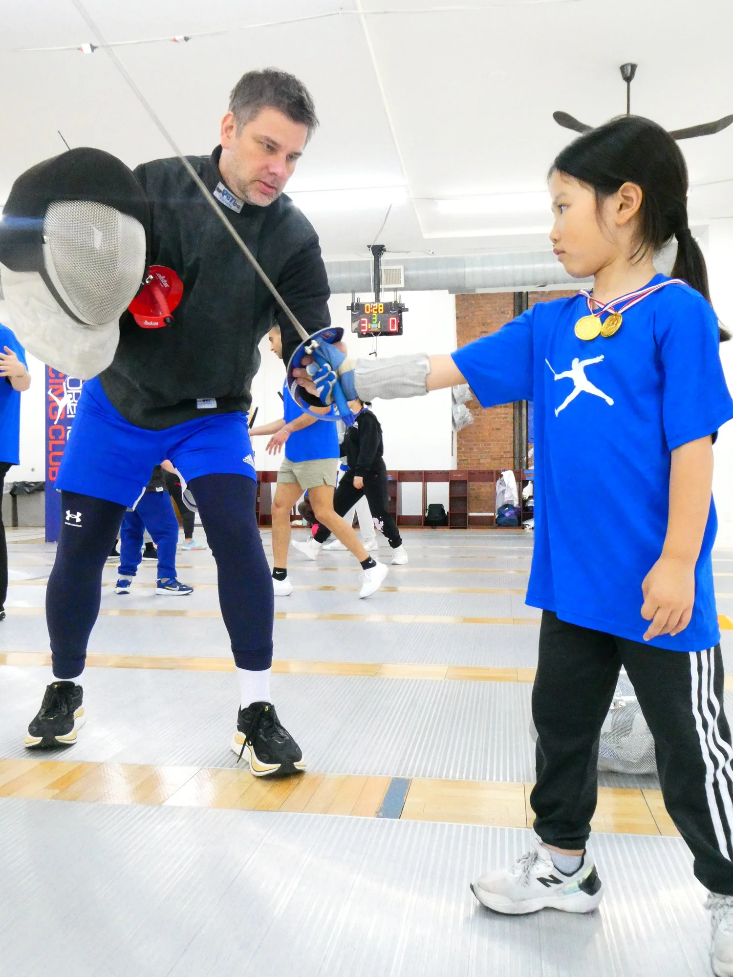 A TMFC coach teaching a young fencer her lunge and saber basics