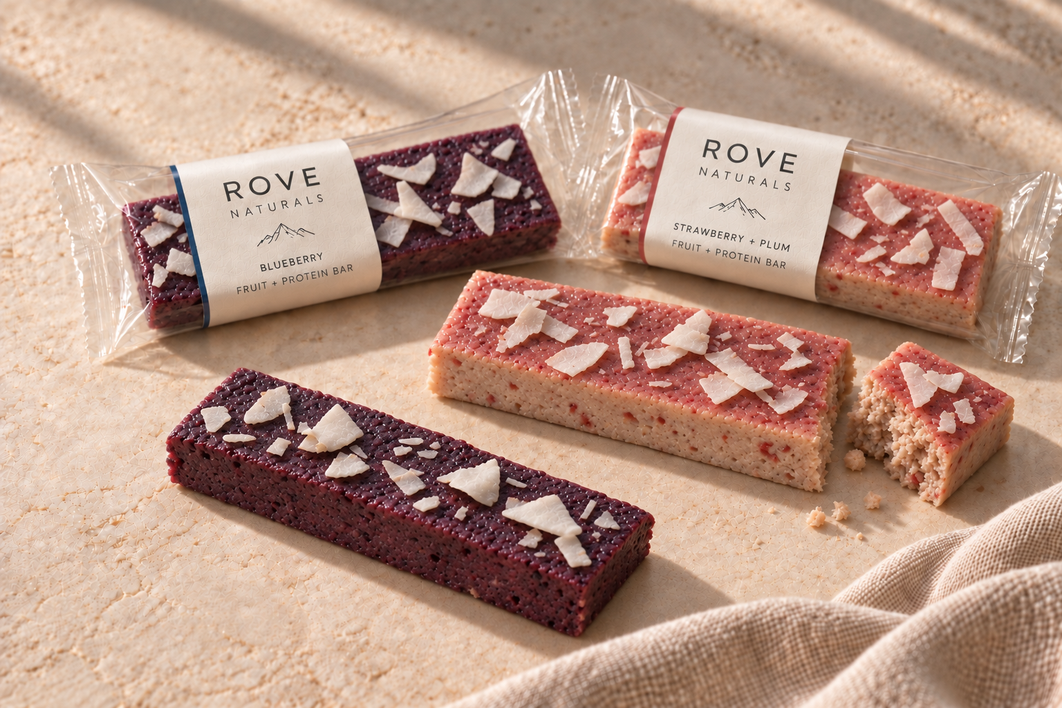 Rove blueberry and strawberry protein bars with a light berry glaze and cracked coconut, beside clear wrappers.