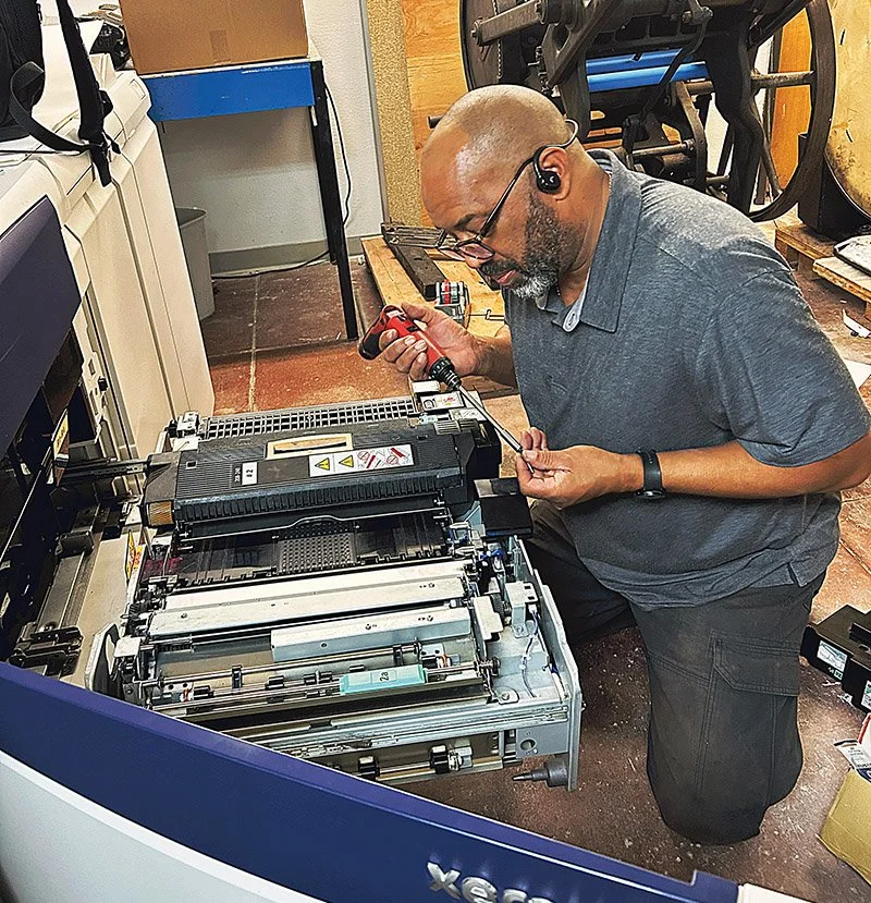 A volunteer print technitian diagnosis and repairs a digital printer