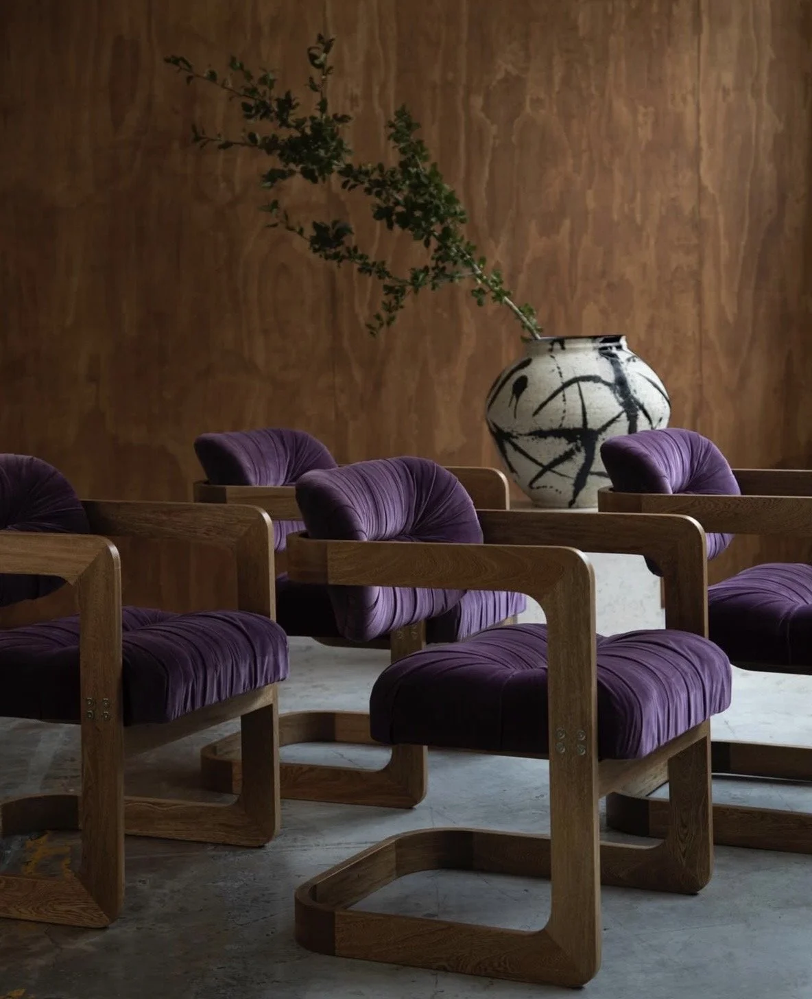 Fauteuils en bois et velours aubergine devant un vase en céramique
