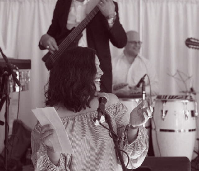 Lissette laughing at the microphone with a band behind her