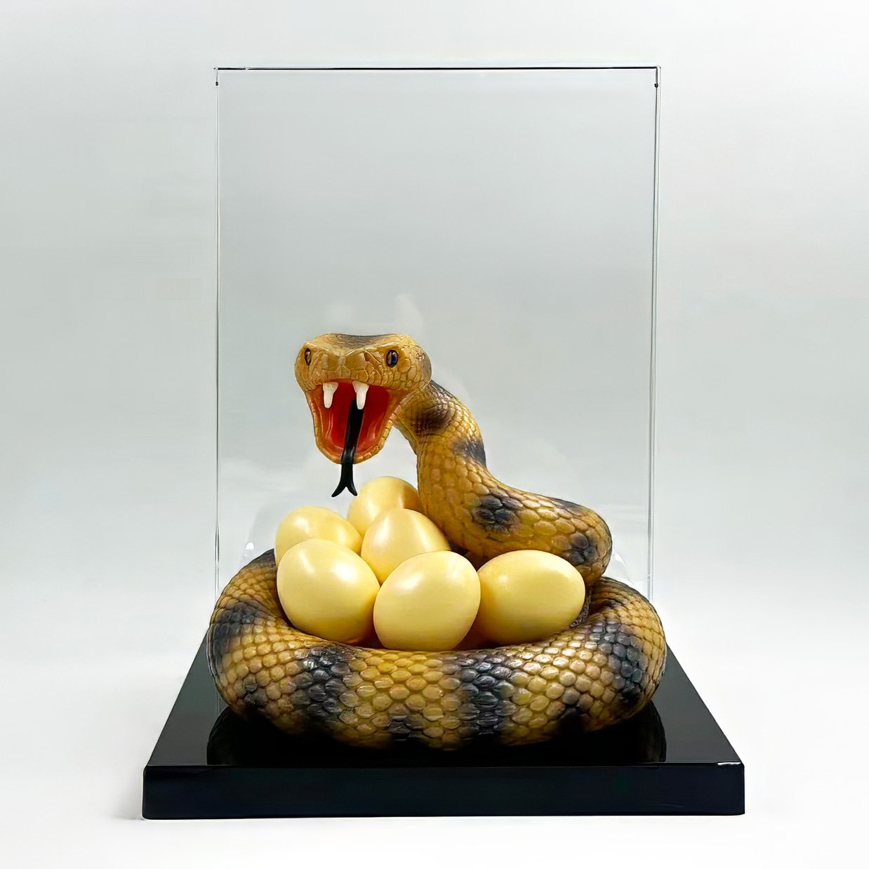 Painted viper sculpture coiled around golden eggs beside a clear panel