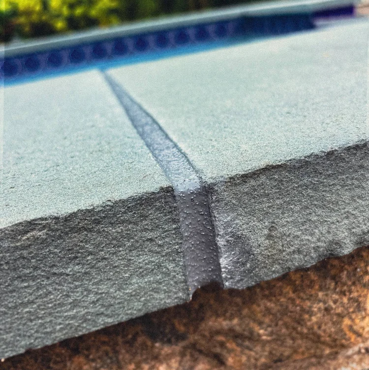 Textured gray sealant at a pool-coping edge.